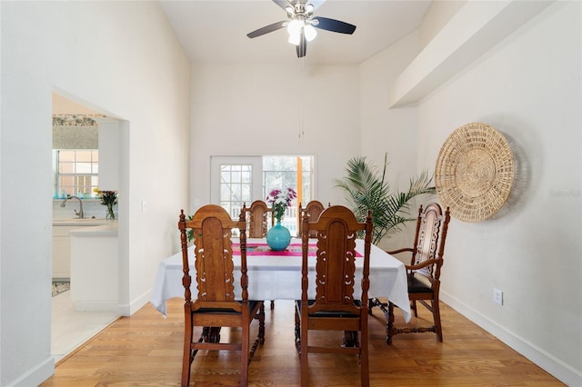 dining room with a ceiling fan, a high ceiling, baseboards, and light wood finished floors