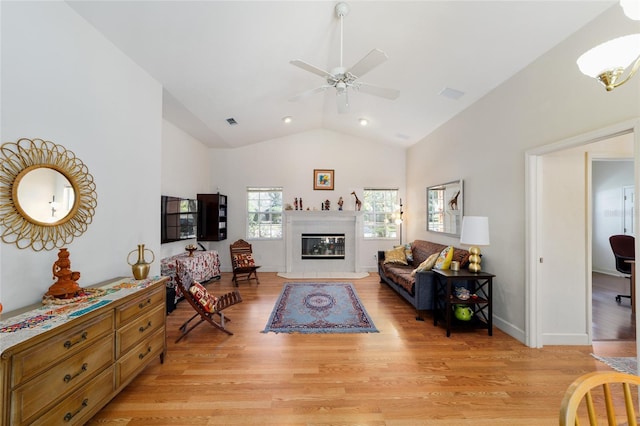 living room featuring light wood-style floors, lofted ceiling, a glass covered fireplace, and visible vents