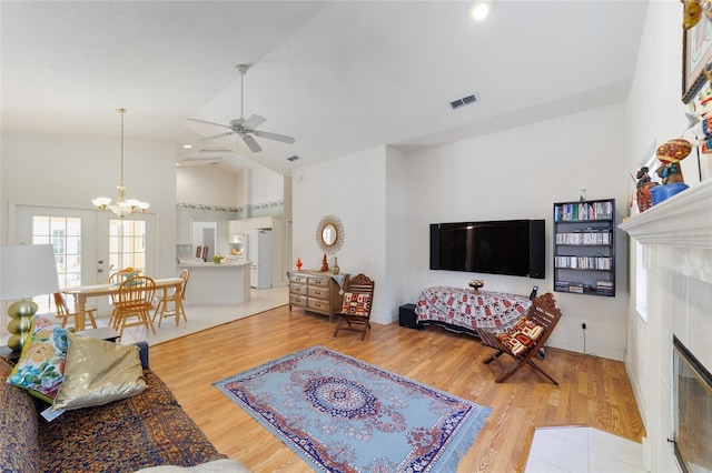 living area with ceiling fan with notable chandelier, visible vents, a tiled fireplace, and wood finished floors