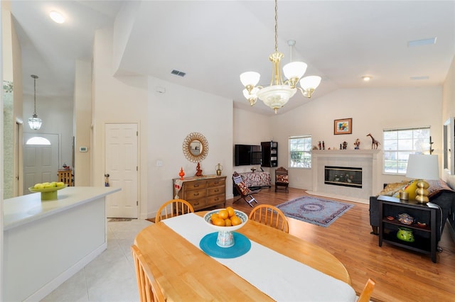 dining room featuring a notable chandelier, light wood finished floors, visible vents, a high end fireplace, and high vaulted ceiling