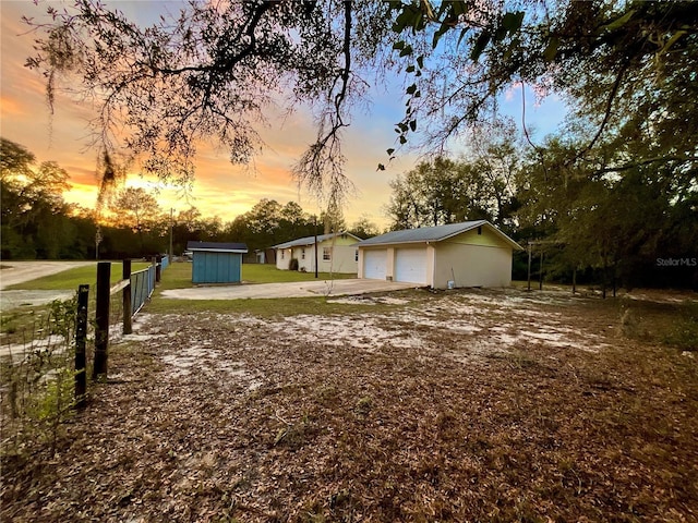 yard at dusk featuring a garage, an outdoor structure, and fence