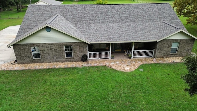 rear view of property with a porch, brick siding, a lawn, and a shingled roof