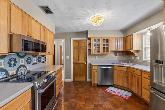 kitchen with light countertops, visible vents, appliances with stainless steel finishes, glass insert cabinets, and a sink