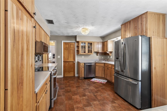 kitchen with appliances with stainless steel finishes, light countertops, visible vents, and glass insert cabinets