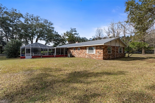 back of property with a yard, brick siding, a chimney, and a lanai