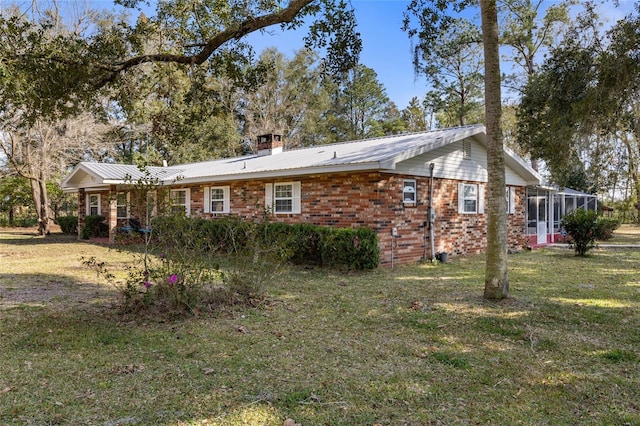 exterior space with metal roof, brick siding, a yard, and a chimney