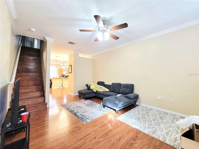 living area featuring wood finished floors, visible vents, crown molding, and stairs