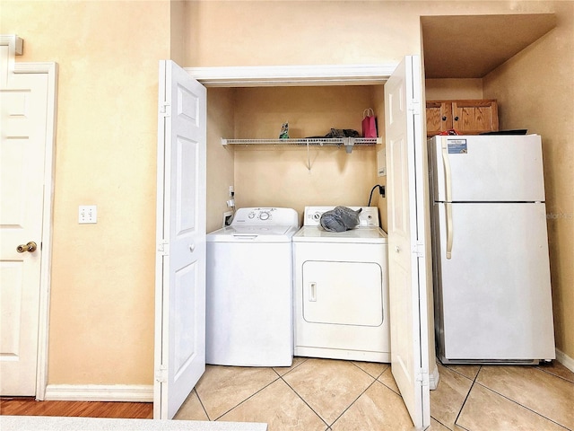 clothes washing area featuring washing machine and dryer, laundry area, baseboards, and light tile patterned floors