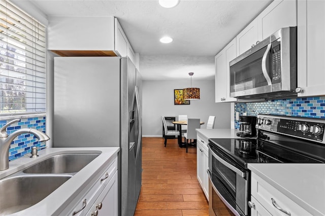 kitchen with stainless steel appliances, wood finished floors, a sink, white cabinetry, and decorative backsplash