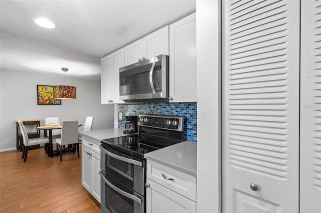 kitchen featuring light wood finished floors, tasteful backsplash, white cabinets, stainless steel appliances, and light countertops