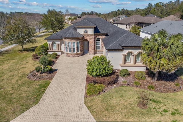 french country home with stone siding, roof with shingles, decorative driveway, and stucco siding