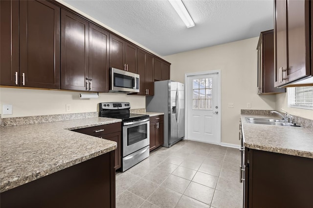 kitchen with light tile patterned floors, appliances with stainless steel finishes, light countertops, dark brown cabinets, and a sink