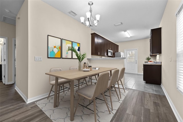 dining space with baseboards, visible vents, a chandelier, and wood finished floors