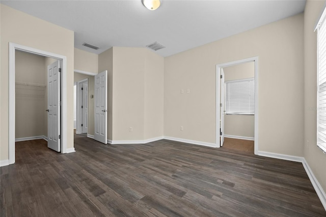 unfurnished bedroom featuring baseboards, visible vents, dark wood finished floors, a walk in closet, and a closet