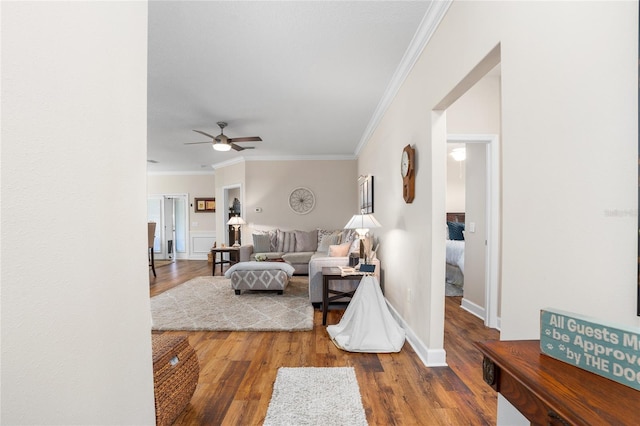 living area with ornamental molding, ceiling fan, baseboards, and wood finished floors