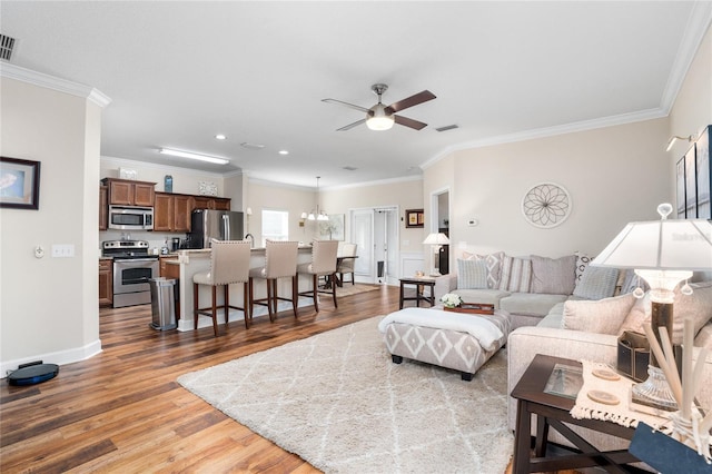 living area featuring ceiling fan with notable chandelier, visible vents, crown molding, and wood finished floors