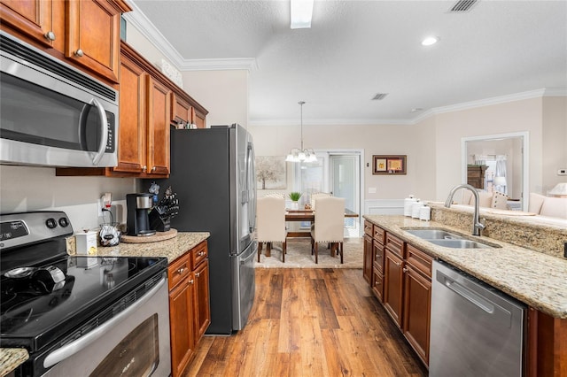 kitchen featuring light stone counters, a sink, ornamental molding, appliances with stainless steel finishes, and brown cabinetry