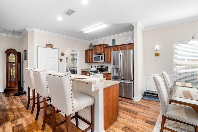 kitchen with visible vents, an island with sink, brown cabinets, a breakfast bar, and stainless steel appliances