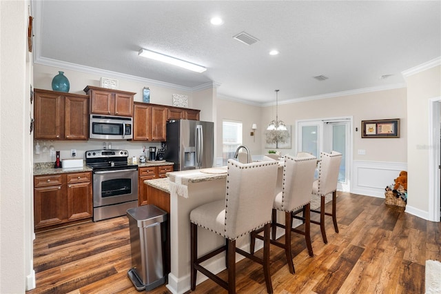 kitchen featuring hanging light fixtures, appliances with stainless steel finishes, a kitchen bar, dark wood finished floors, and a center island with sink