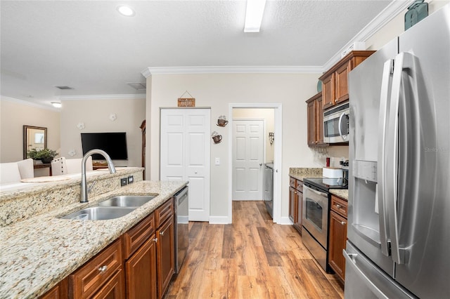 kitchen featuring light stone countertops, appliances with stainless steel finishes, a sink, and ornamental molding