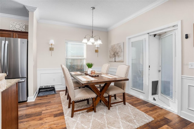 dining area with a wainscoted wall, crown molding, a decorative wall, an inviting chandelier, and wood finished floors