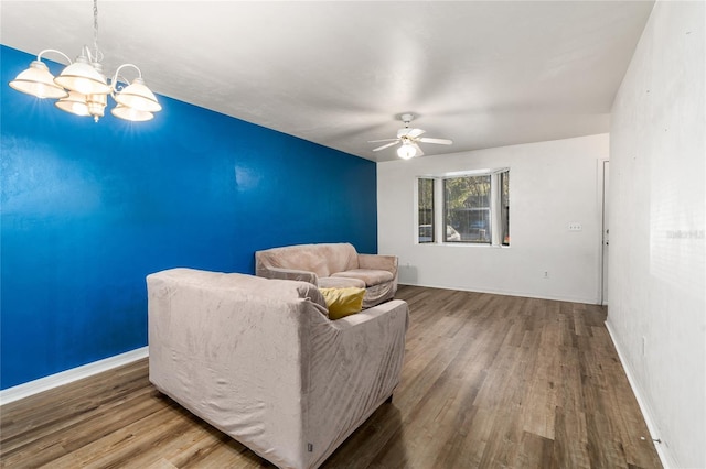 sitting room with baseboards, wood finished floors, and ceiling fan with notable chandelier