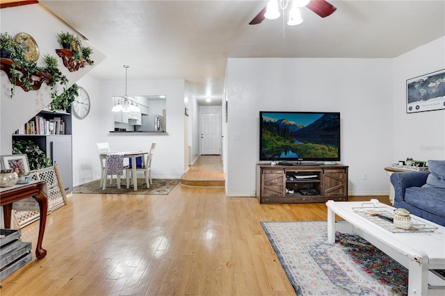 living area with light wood-type flooring, baseboards, and ceiling fan with notable chandelier