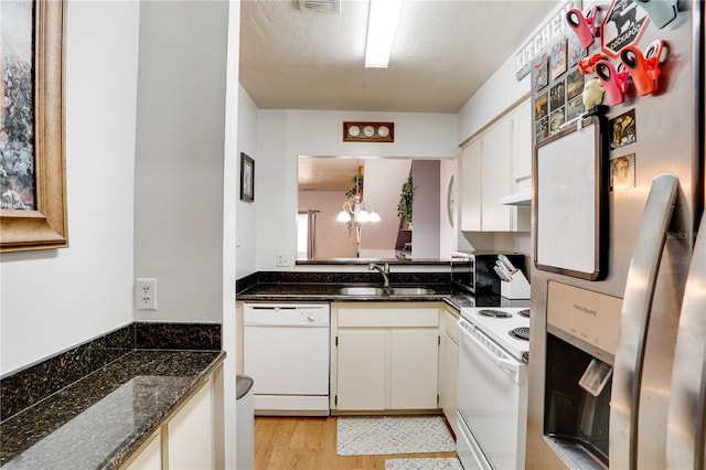 kitchen featuring under cabinet range hood, white appliances, a sink, white cabinetry, and dark stone counters