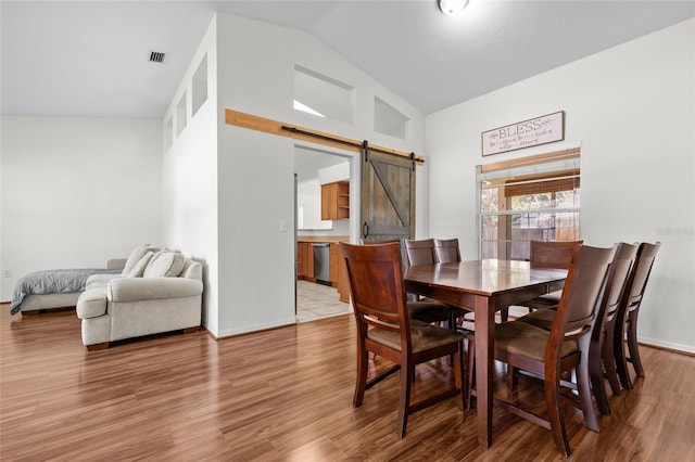 dining space with high vaulted ceiling, a barn door, wood finished floors, visible vents, and baseboards