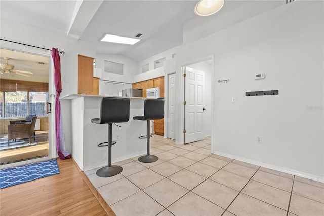 kitchen featuring lofted ceiling, white microwave, a ceiling fan, a kitchen breakfast bar, and freestanding refrigerator