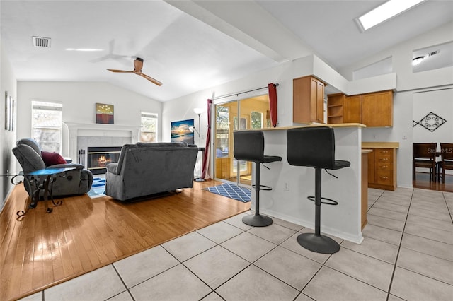 living area with light tile patterned floors, visible vents, a ceiling fan, vaulted ceiling, and a glass covered fireplace