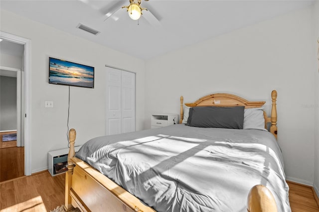 bedroom with a closet, wood finished floors, visible vents, and a ceiling fan