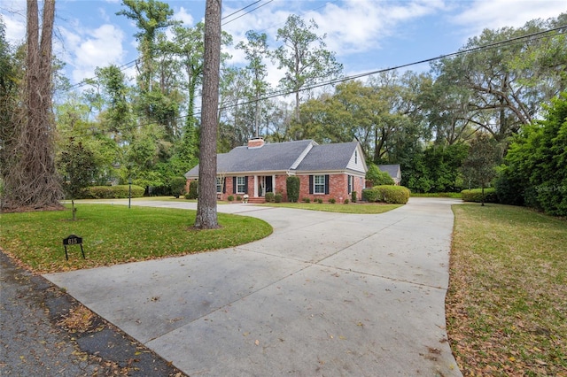 view of front of property with brick siding, a chimney, curved driveway, and a front yard