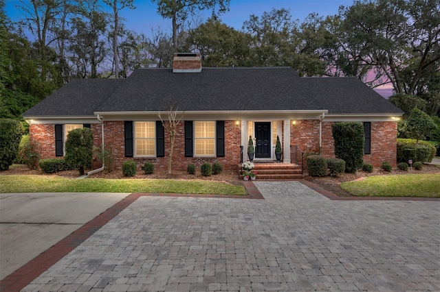 view of front facade featuring brick siding, a chimney, and a shingled roof