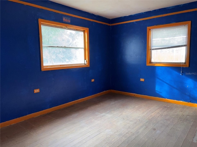 empty room with baseboards, wood finished floors, and a healthy amount of sunlight