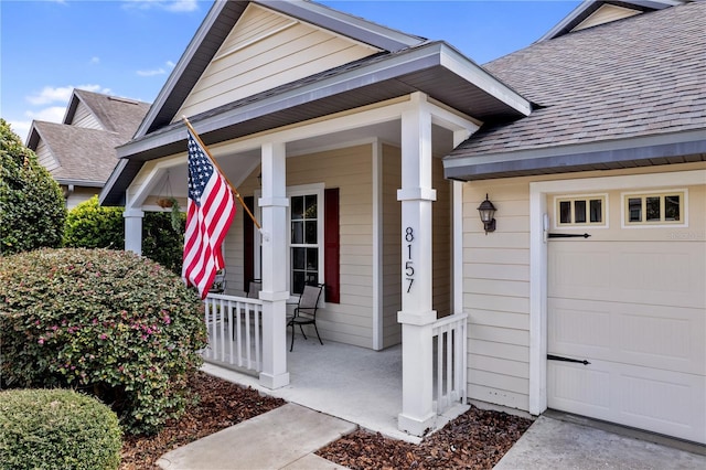 doorway to property featuring an attached garage, a porch, and roof with shingles