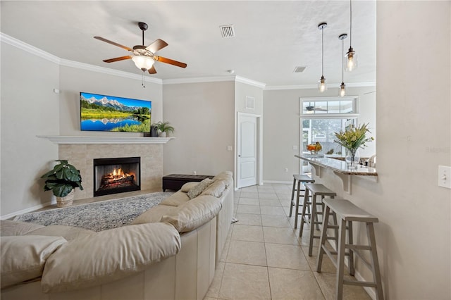 living area featuring visible vents, crown molding, a tiled fireplace, and light tile patterned floors