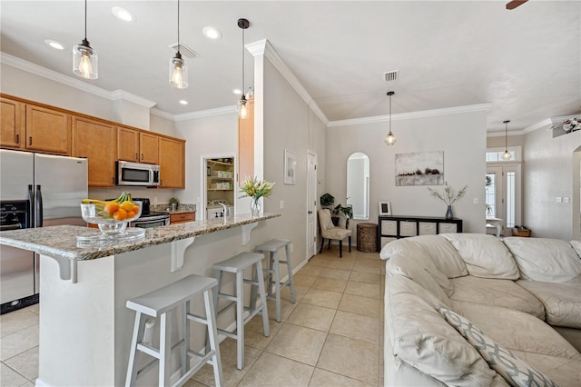 kitchen with light tile patterned floors, arched walkways, appliances with stainless steel finishes, open floor plan, and a kitchen bar