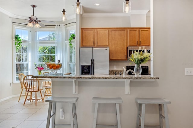 kitchen with light stone counters, ornamental molding, appliances with stainless steel finishes, brown cabinets, and a kitchen bar