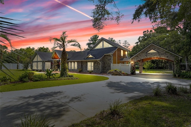 view of front facade with driveway, a front lawn, stone siding, and fence