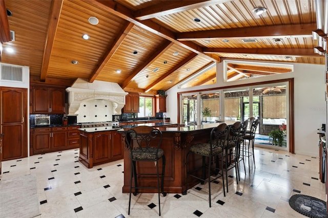 kitchen featuring lofted ceiling with beams, premium range hood, a kitchen island, visible vents, and dark countertops