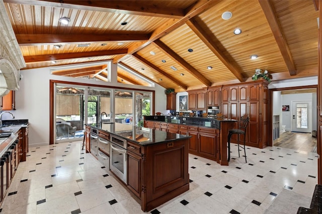 kitchen featuring lofted ceiling with beams, wooden ceiling, a sink, stainless steel oven, and a large island with sink