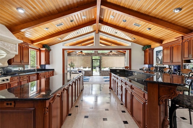 kitchen with a large island, brown cabinets, open floor plan, vaulted ceiling with beams, and a sink