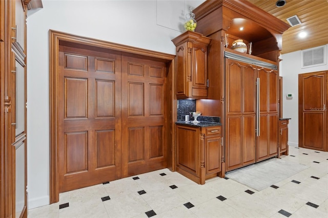 kitchen with dark stone counters, brown cabinetry, backsplash, and visible vents