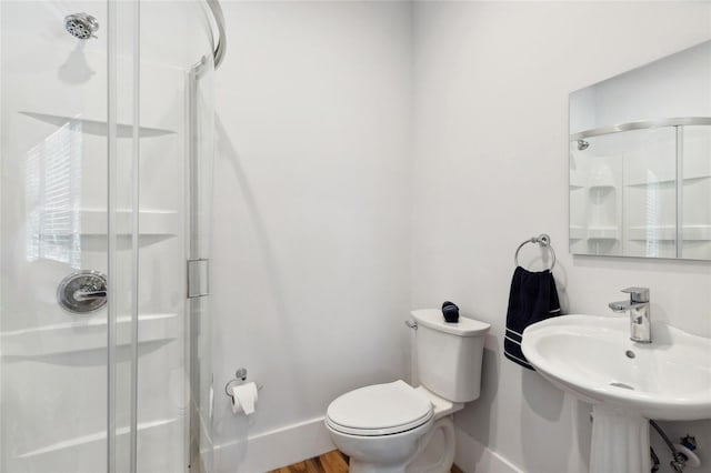 bathroom featuring toilet, wood finished floors, a sink, baseboards, and a stall shower