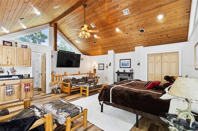 bedroom featuring high vaulted ceiling, a stone fireplace, light wood-style flooring, and visible vents