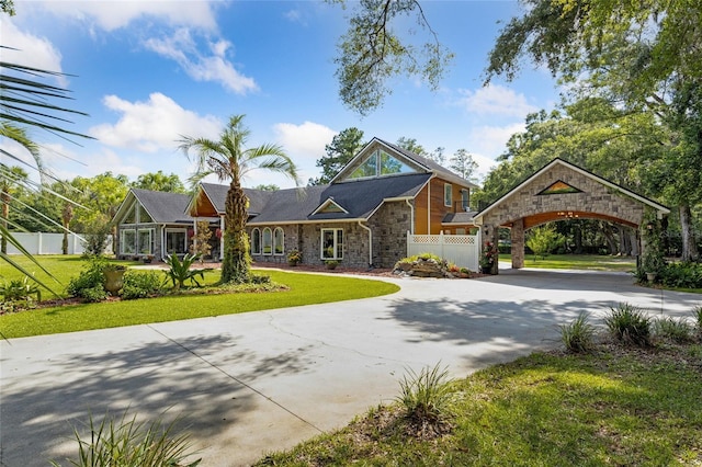 view of front facade featuring driveway, stone siding, fence, and a front yard