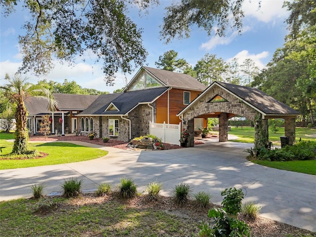 view of front of house featuring stone siding, fence, concrete driveway, and a front yard