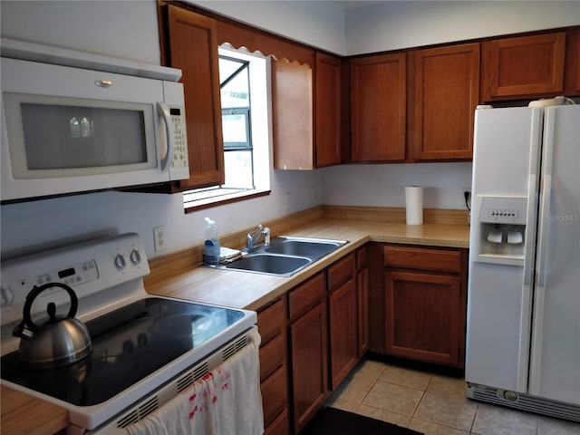 kitchen featuring white appliances, light countertops, brown cabinets, a sink, and light tile patterned floors