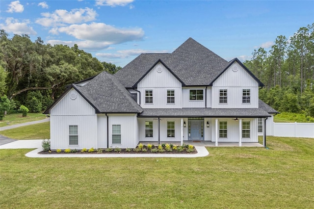 modern farmhouse featuring a front yard, covered porch, roof with shingles, and fence